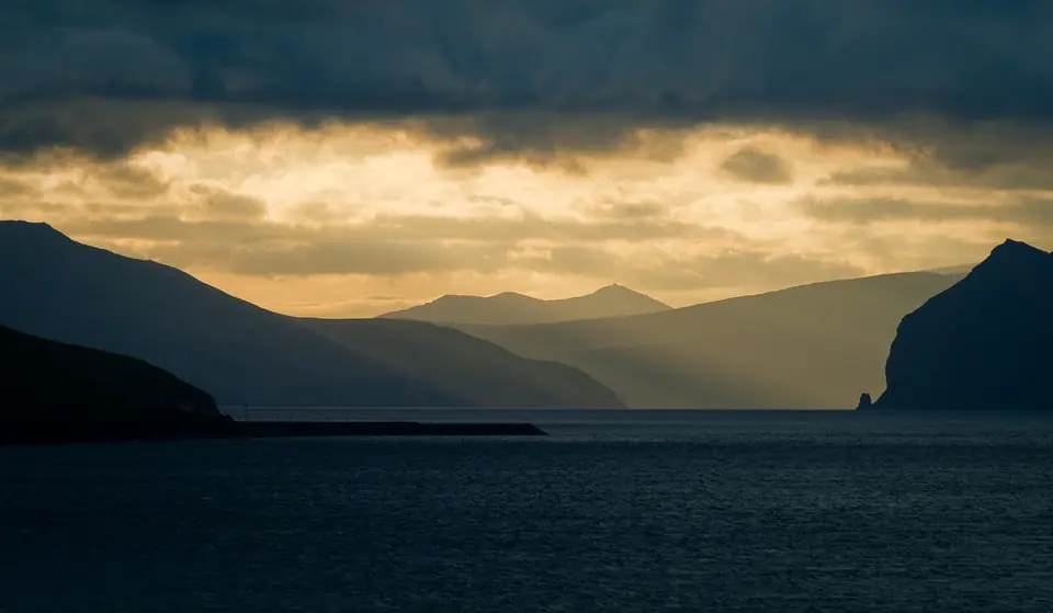 Fjord und Berge der Färöer unter schweren Wolken mit durchbrechendem Licht