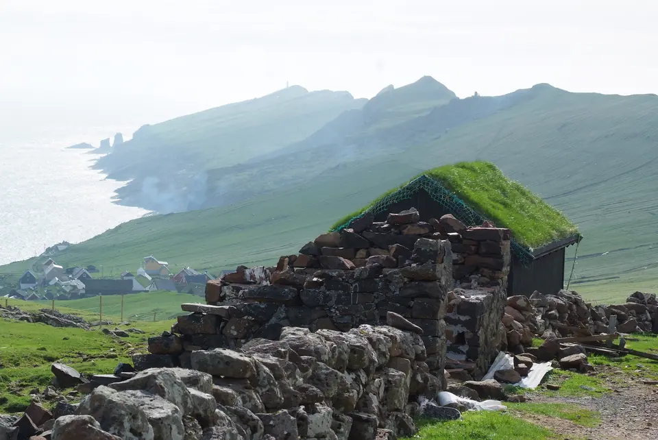 Gammelt steinhus med torvtak på Mykines med fjellene bak