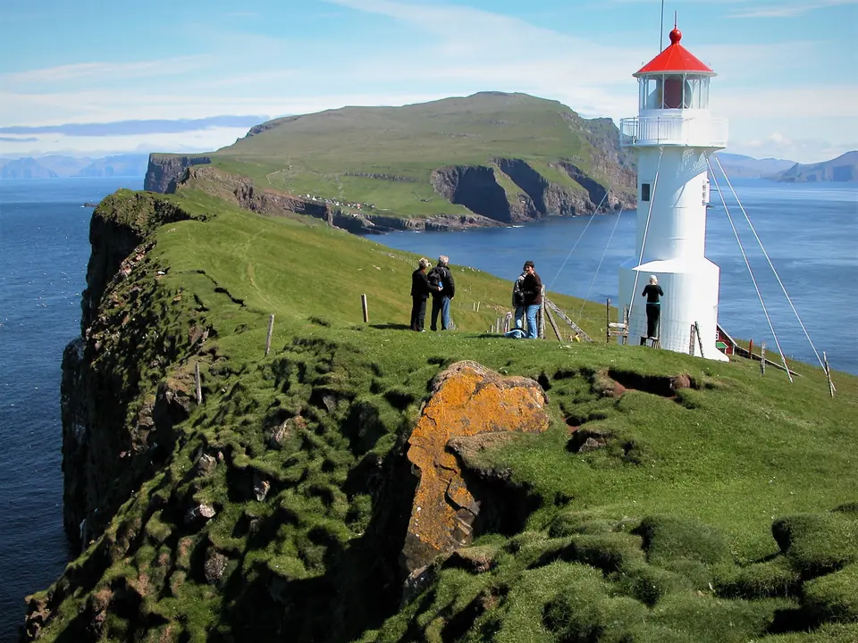 Der weiße Leuchtturm auf Mykineshólmur mit Wanderern auf dem Weg