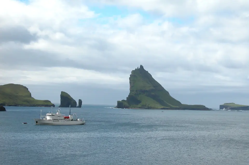 Ein Boot fährt an Tindhólmur und den Drangarnir vorbei