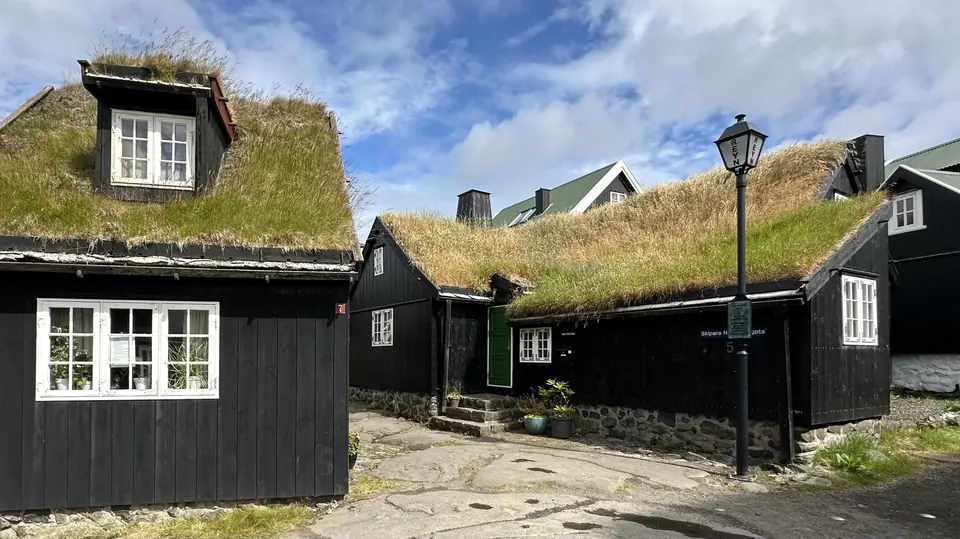 Svarta trähus med torvtak och gatlykta på Tinganes